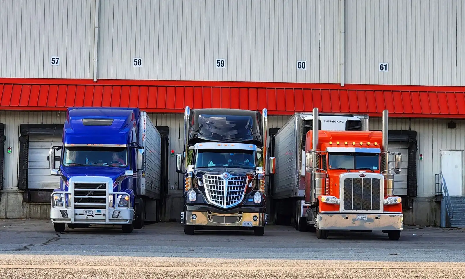 Three trucks facing forward outside of a warehouse loading dock with a red awning.
